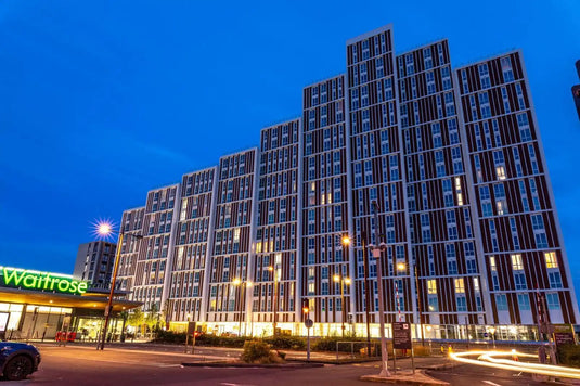 Modern glass and steel apartment building with illuminated windows at dusk.